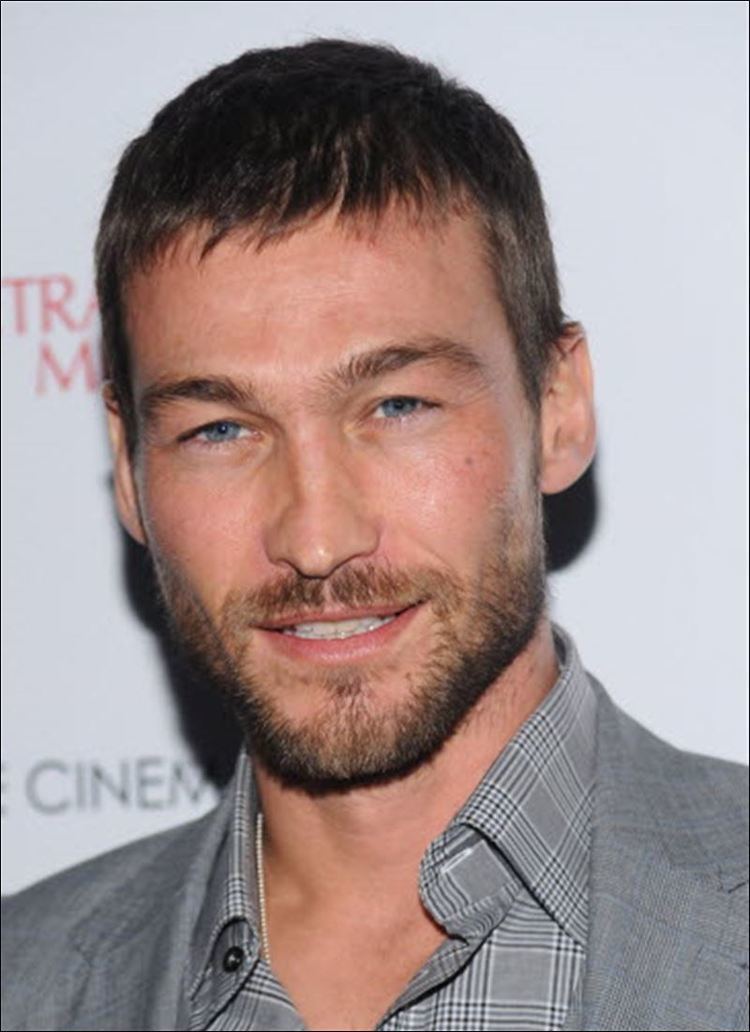 Andy Whitfield smiling, with beard and mustache, and wearing a gray suit and checkered long sleeves.