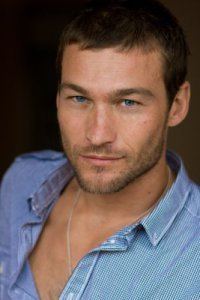 Andy Whitfield with a serious face, with a beard and mustache, wearing a necklace and blue polo shirt.