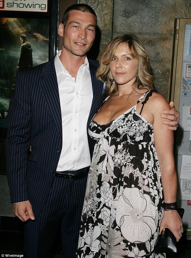 Andy Whitfield smiling with his wife Vashti Whitfield while wearing white long sleeves, a striped black suit, and striped black pants.