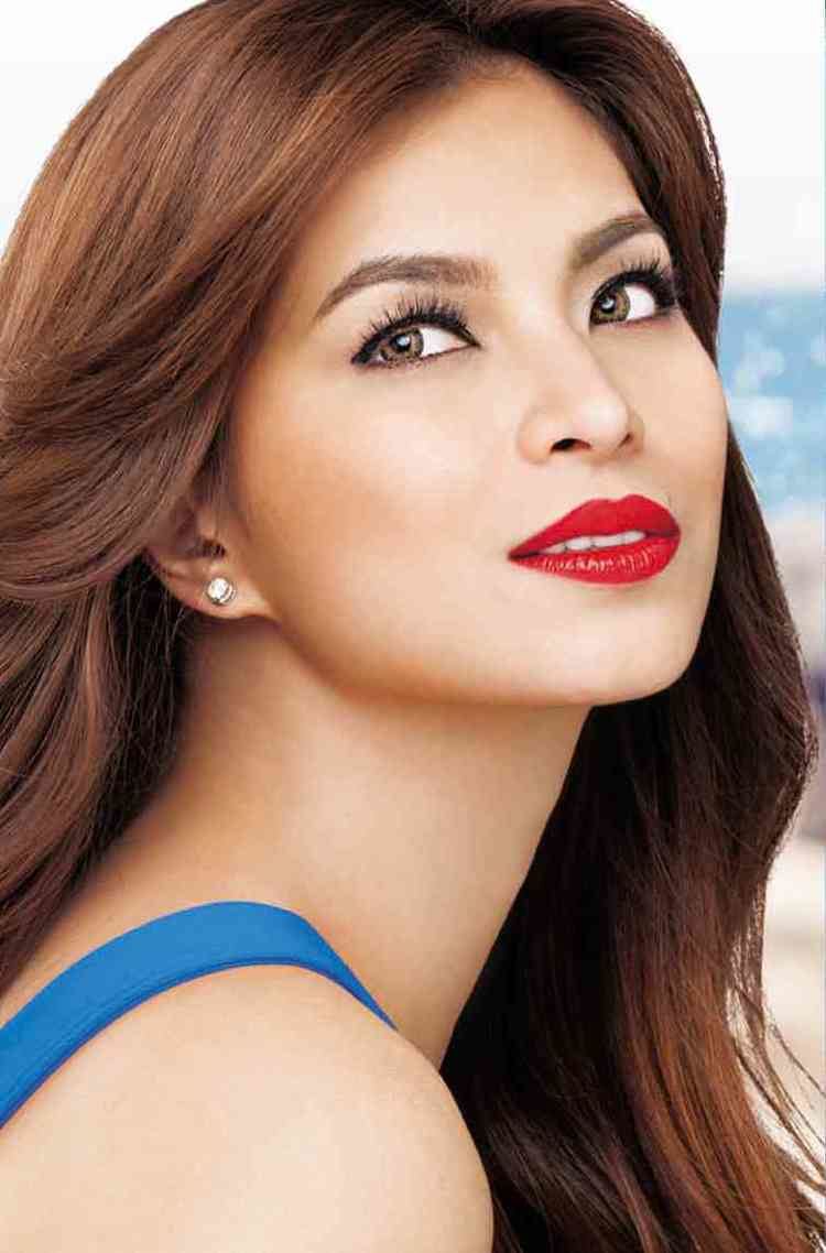 Angel Locsin smiling while looking up and wearing a blue sleeveless top and earrings