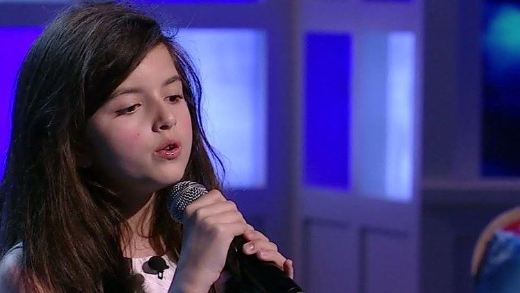 Angelina Jordan holding a microphone while singing
