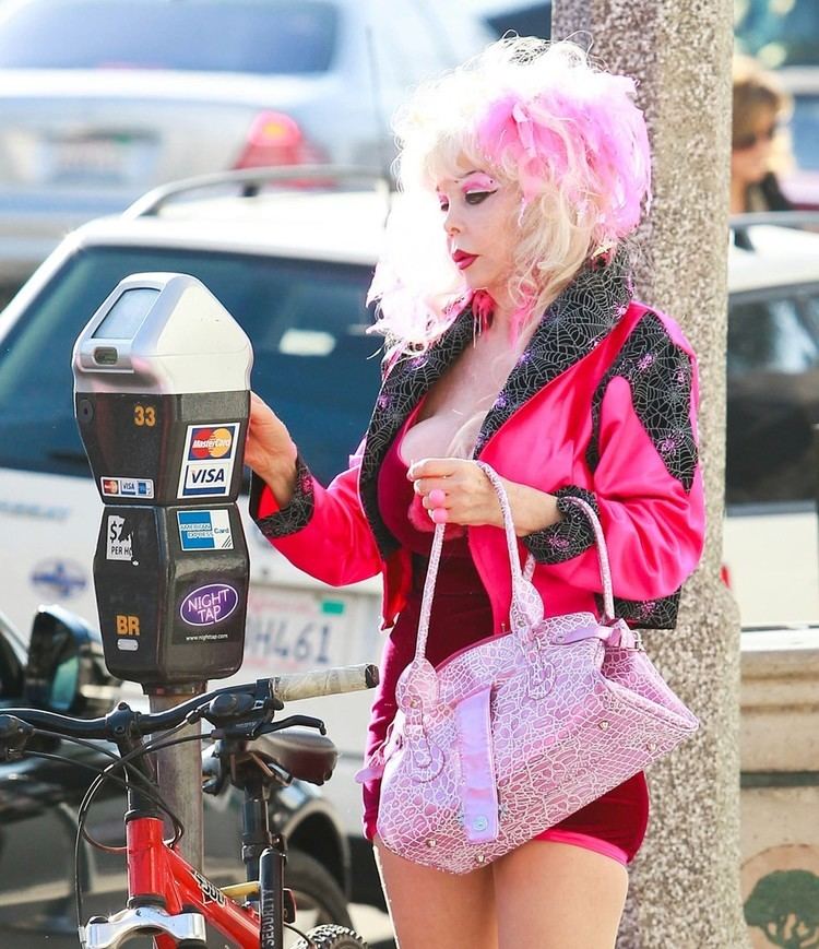 Angelyne wearing black and pink jacket paired with red mini dress and pink bag as she swipes her atm card