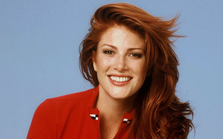 Angie Everhart smiling with orange-brown wavy hair while wearing a red blouse