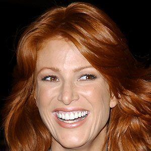 Angie Everhart smiling while looking at something with orange-brown wavy hair