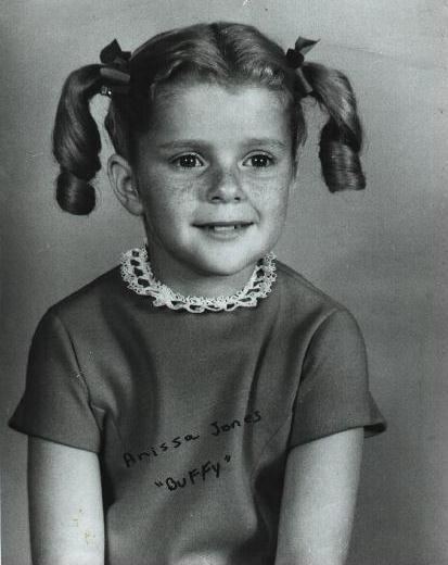 Anissa Jones smiling and sporting two ears hairstyle with black ribbons while wearing a short sleeve blouse.