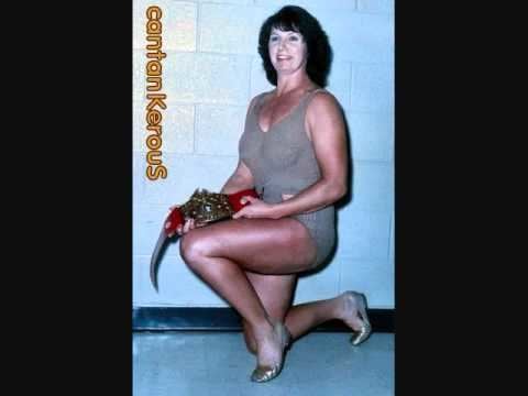 Ann Casey posing with one knee down and holding her title belt and wearing wrestling attire.