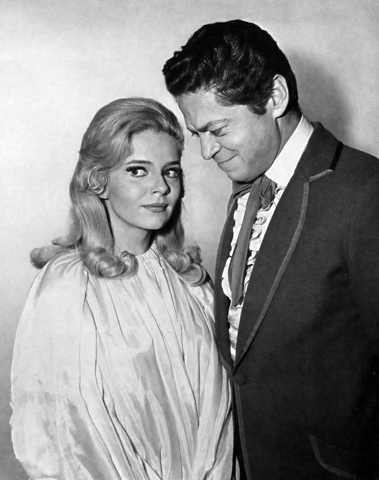 Ann Elder smiling and wearing a long sleeves dress while Ross Martin looking at her and wearing a coat, long sleeves, and a vest