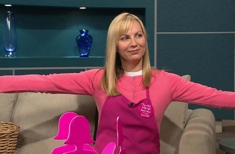 Ann-Maree Biggar' s arms open while wearing pink long sleeves and apron