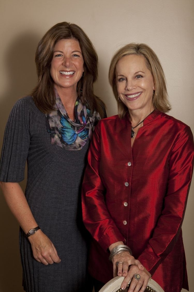 Ann Maurice smiling, with blonde hair and wearing a red dress with Tracy Metro smiling, with wavy hair and wearing a gray dress.