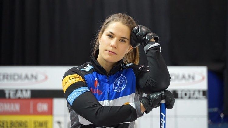 Anna Hasselborg looking fierce with hand on head and holding a curling broom while wearing a jacket and gloves