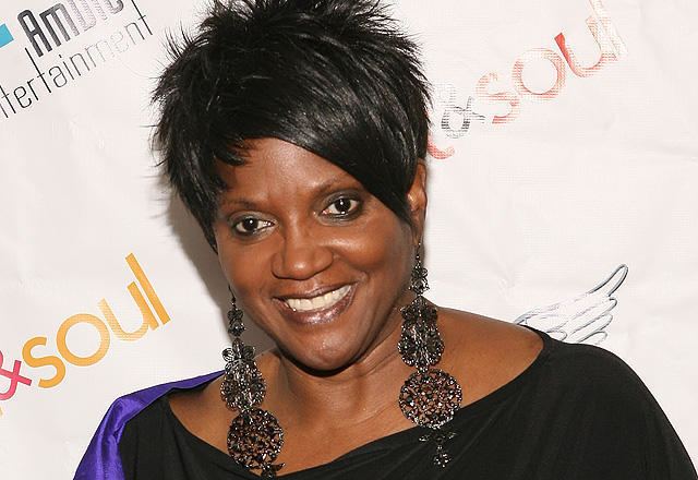 Anna Maria Horsford smiling while wearing a big necklace, earrings, and black blouse