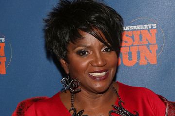 Anna Maria Horsford smiling while wearing a red dress, earrings and necklace