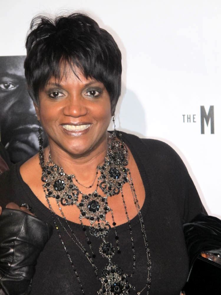 Anna Maria Horsford smiling while wearing a big necklace, earrings, and black blouse