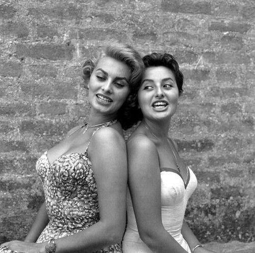 Sophia Loren smiling and wearing a floral dress while Anna Maria Villani Scicolone wearing a plain dress with a sweetheart neckline
