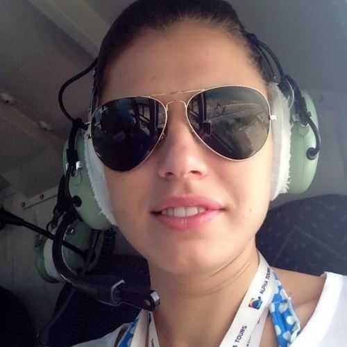 Anna Petrakova smiling while riding a chopper, wearing ID cards ribbons, sunglasses, headset, and a white blouse