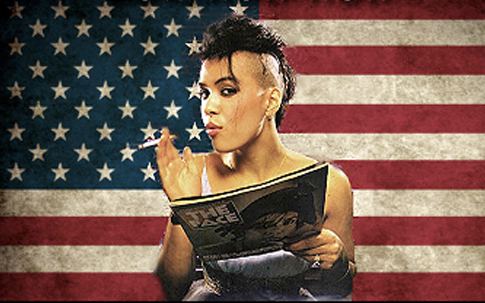 Annabella Lwin posing in front of camera looking to her left while holding magazine of her left hand and cigarette on her right hand with fade haircut style, wearing two rings and a bracelet