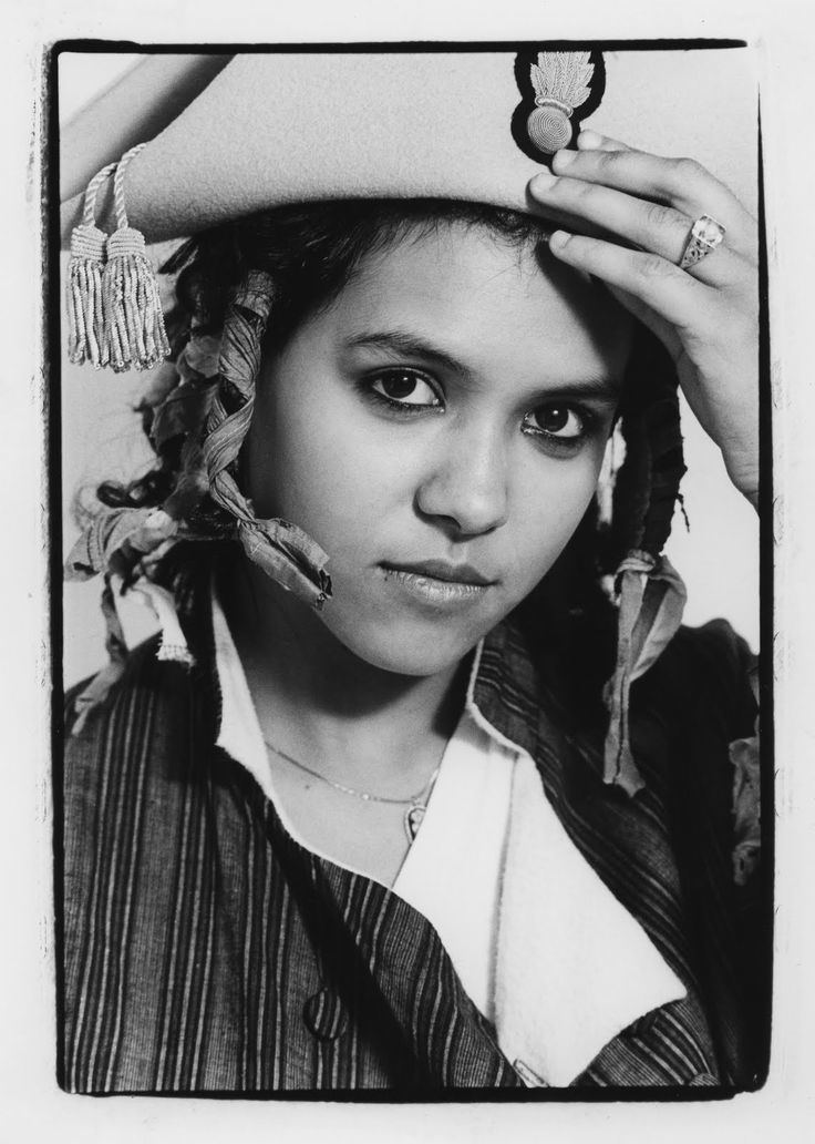 Annabella Lwin with tight lipped smile, wearing a white cap, a ring and a necklace, tied her hairs with ribbons, wearing a black and white uniform