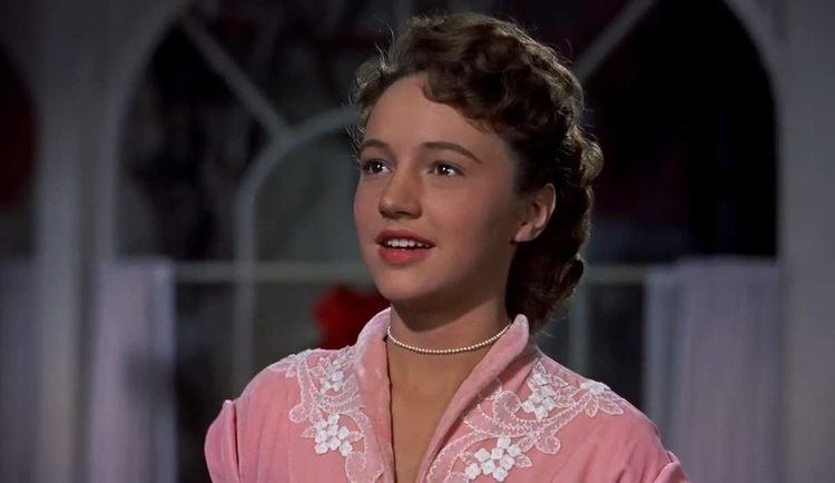 Anne Whitfield smiling and looking at someone while wearing a pink blouse in a scene from the 1954 American musical film, White Christmas