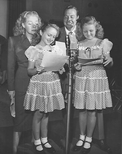 Alice Faye and Phil Harris with their radio daughters, Anne-Whitfield and Jeanine Roose are smiling while looking at the script