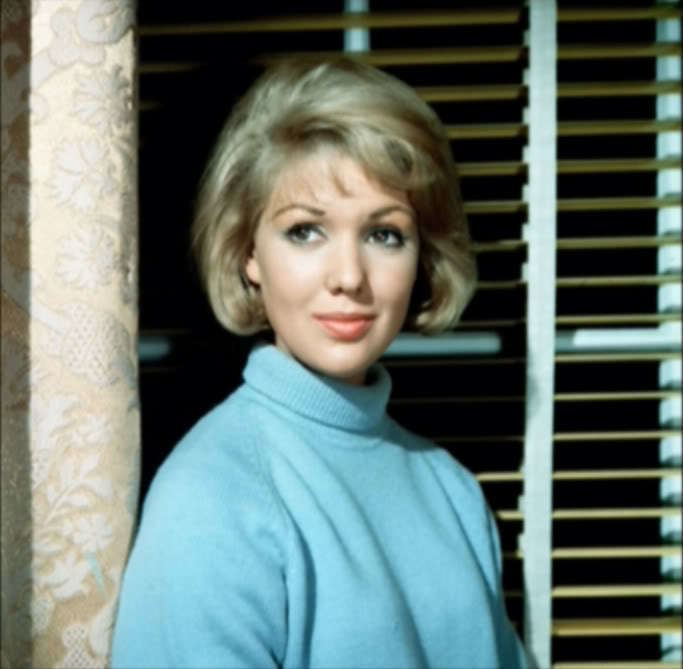 Annette Andre with a tight-lipped smile and short blonde hair while wearing a blue turtle-neck blouse