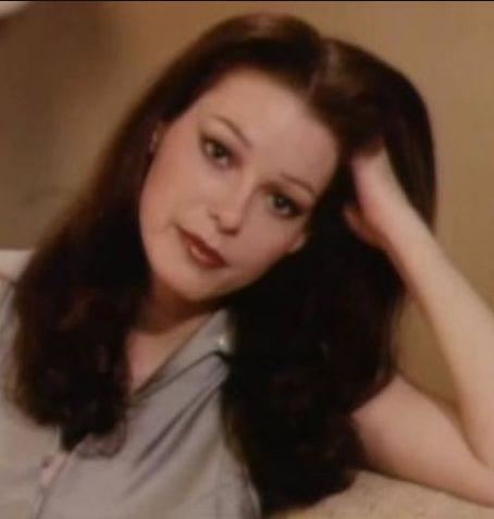 Annette Haven's head leaning on her hand while wearing a gray blouse