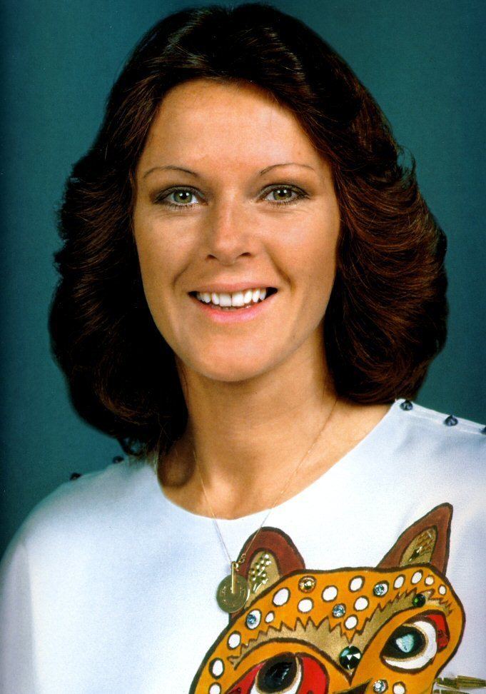 Anni-Frid Lyngstad smiling while wearing a white blouse with owl embroidery and necklace