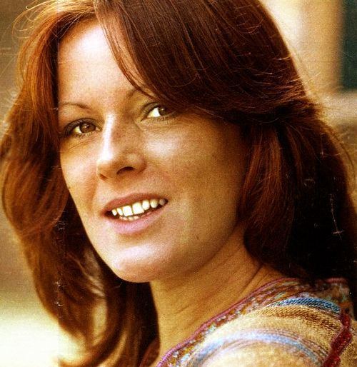 Young Anni-Frid Lyngstad smiling while wearing a brown and blue blouse