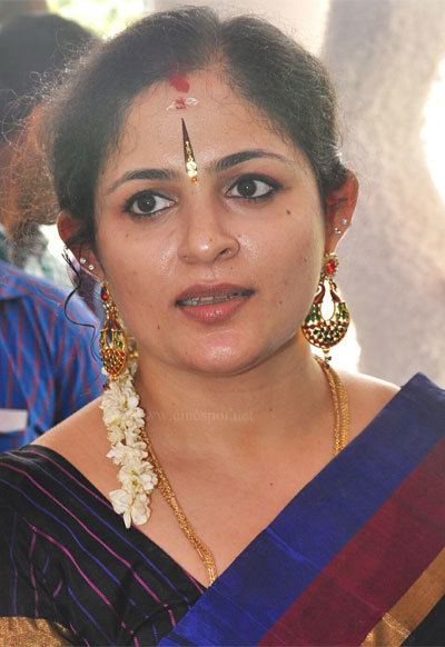 Annie with bindis on her forehead while wearing gajra, earrings, necklace, black dress with a combination of the color blue, gold, and maroon