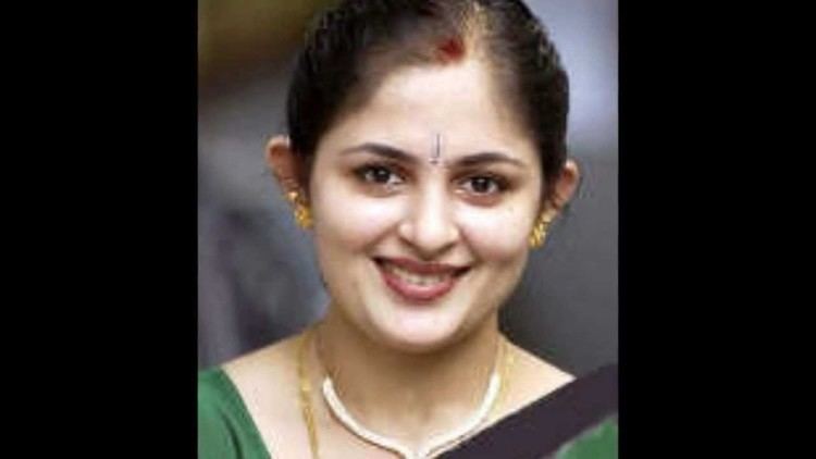 Annie smiling with bindis on her forehead while wearing a green and black blouse, necklace, and earrings