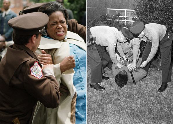 On the left, Oprah Winfrey as Annie Lee Cooper with a struggling face while being dragged by the uniformed policemen with people in the background in a movie scene from "Selma", a 2014 American historical drama film. On the right, Oprah Winfrey as Annie Lee Cooper lying and resisting on the grassy ground while holding a billy club while being forcefully arrested and handcuffed by three uniformed policemen with plants and a window in the background in a movie scene from "Selma", a 2014 American historical drama film. On the left, Oprah is wearing a cream wide-collared coat over a blue buttoned dress while on the right, Oprah is wearing a long-sleeve dress while the three policemen have belts with guns in their holsters, socks, and formal shoes, wearing long-sleeve uniforms and slacks.