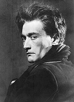 Antonin Artaud looking at the back while wearing a black blazer and scarf