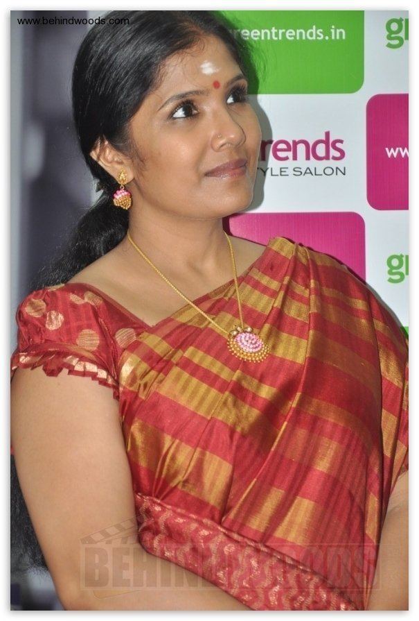 Anuradha Sriram smiling while looking afar and wearing a red and gold dress, earrings, and necklace