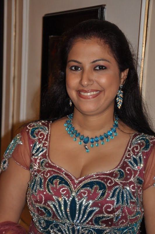 Anusha smiling while wearing a maroon and blue dress, blue necklace, and earrings