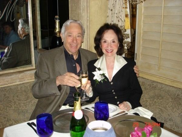 April Stevens holding a glass of wine while wearing black and cream dress with Nino Tempo in his brown coat and black long sleeves