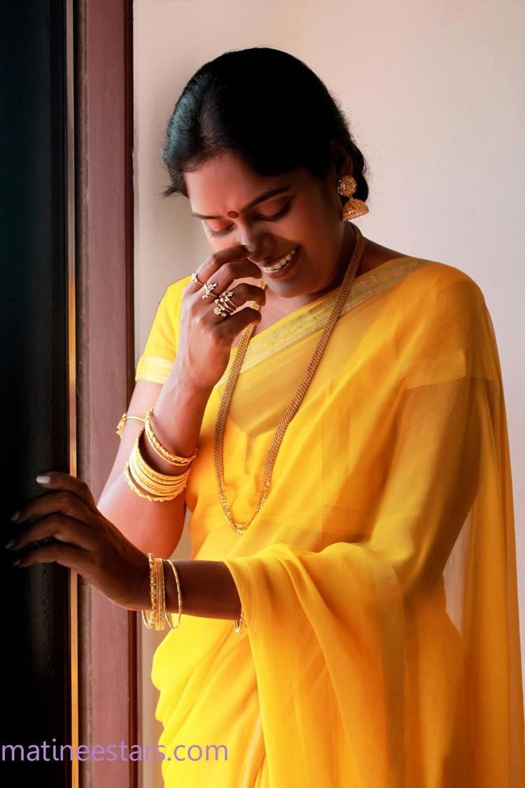 Archana (actress) wearing earrings, a gold necklace, rings, bracelets, and a yellow dress.