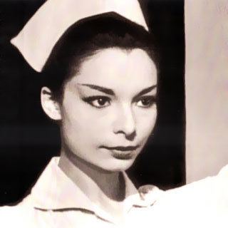 Arlene Martel looking serious and wearing a nurse dress and a white cap