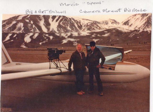 Bill (left) is serious, has white hair, wearing a brown jacket and black pants and brown shoes, left hand on the wing of the plane, and has an IMAX camera on the left wing. Arthur Everett Scholl( left) is serious, wearing a black cap, black shades, a black jacket and pants, and brown shoes, both hands on his waist.