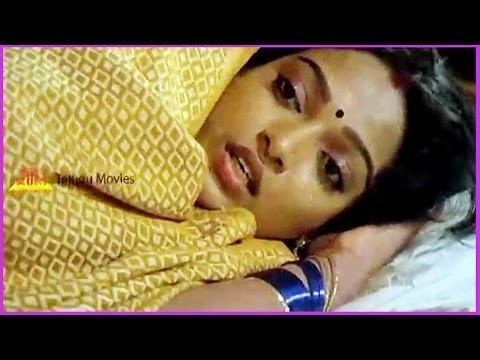 Aruna Mucherla is sad, mouth half open, lying with her left hand underneath her head. has black long hair, a bindi on forehead, wearing a gold earrings, gold bracelet, blue bracelet, and Gold saree,