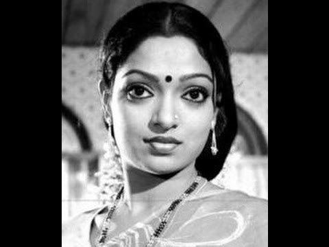 Aruna Mucherla is serious, standing in a room in black and white, has black long hair, a bindi on forehead, nose piercing, wearing a necklace, earrings and saree.