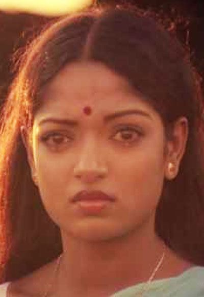 Aruna Mucherla is sad, has black long hair, a bindi on forehead, wearing a gold necklace, earrings and blue saree.