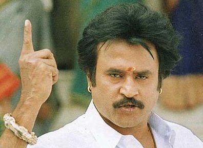 Rajinikanth as Arunachalam with a serious face while pointing his finger above, wearing earrings, bracelets, and a white long sleeve in a movie scene from Arunachalam, a 1997 Indian Tamil-language action drama film.