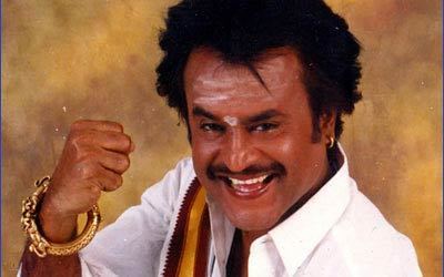 Rajinikanth as Arunachalam smiling while doing a ready-to-punch gesture scarf on his shoulder, wearing bracelets, and a white long sleeve.