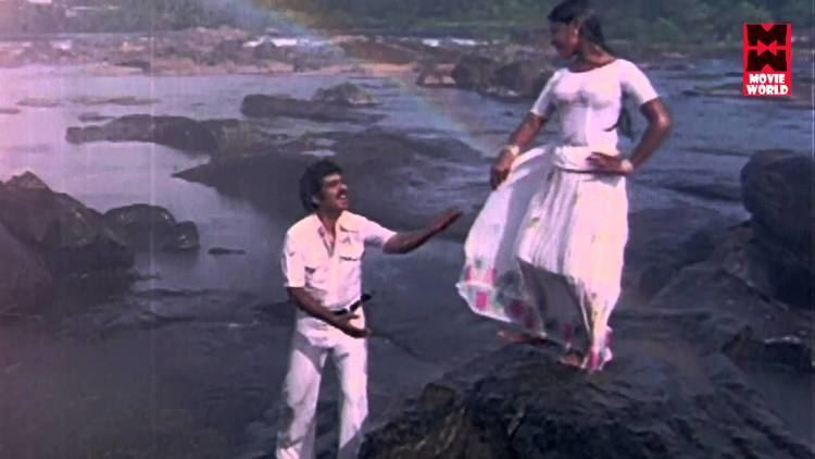 Srividya standing on a big rock at the beach while Raveendran holding her hand and she wearing a white long dress in the music video of the 1980 film, Ashwaradham