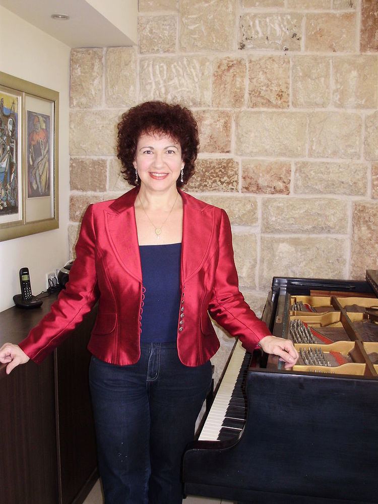 A woman standing in her house, next to a piano