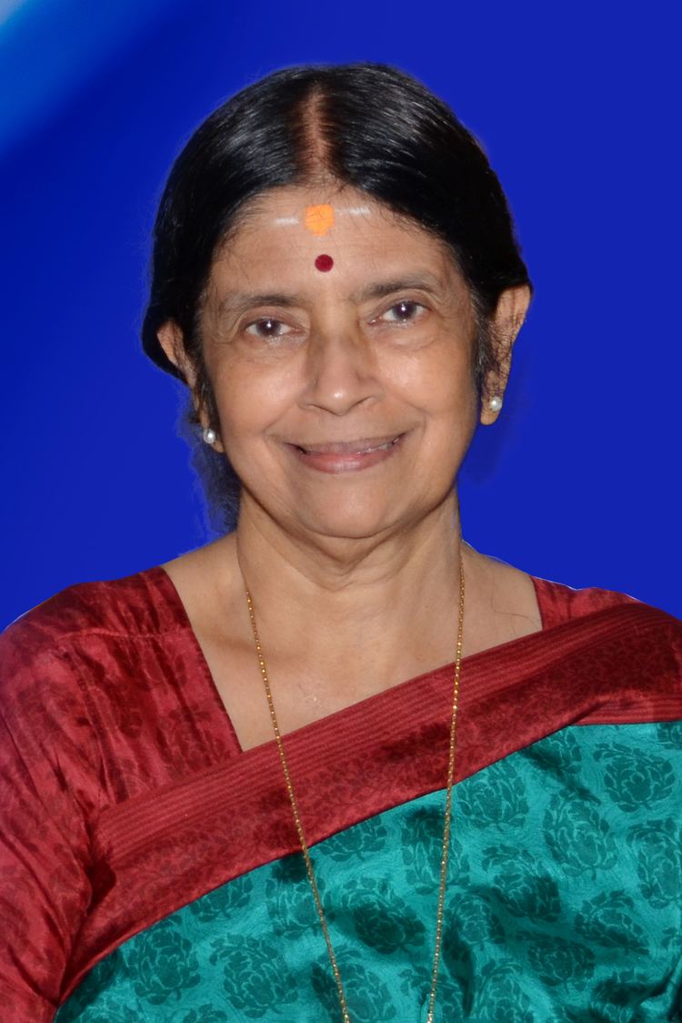 Aswathi Thirunal Gowri Lakshmi Bayi smiling while wearing a red and blue dress, pearl earrings, and gold necklace