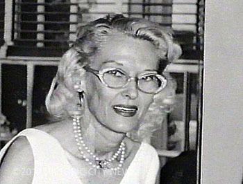Athalia Ponsell Lindsley smiling, with curly white hair, wearing eyeglasses, earrings, a pearl necklace, and a white sleeveless top.
