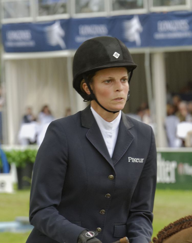 Athina Onassis Roussel riding on a horse while wearing black coat, white inner blouse and black helmet