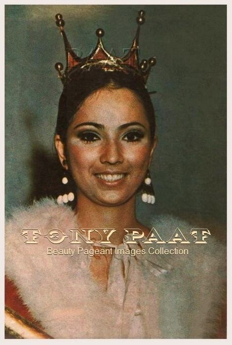 Aurora Pijuan smiling, wearing a crown, earrings, and a red and white fur coat.