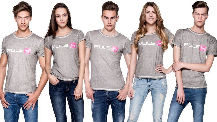 Five aspiring models compete for the title of Austria's Next Topmodel. Some are smiling and others having a fierce look while wearing denim pants and gray shirts with PULS print at the center