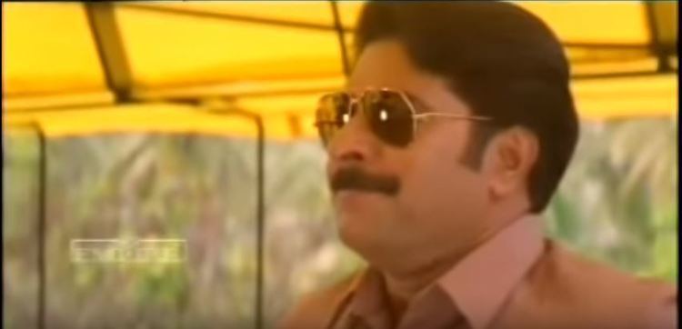 Mammootty looking afar while wearing sunglasses and brown polo in a scene from the 1996 film, Azhakiya Ravanan